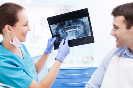 A woman is sitting in a dental chair while a dentist examines her teeth.