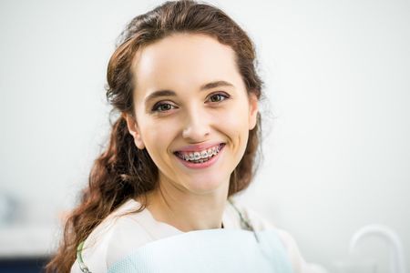 A woman with braces is smiling while sitting in a dental chair.