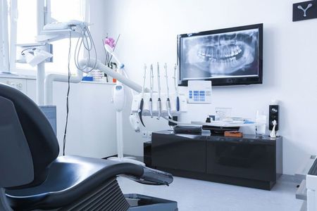 A dental office with a dental chair and a television on the wall.