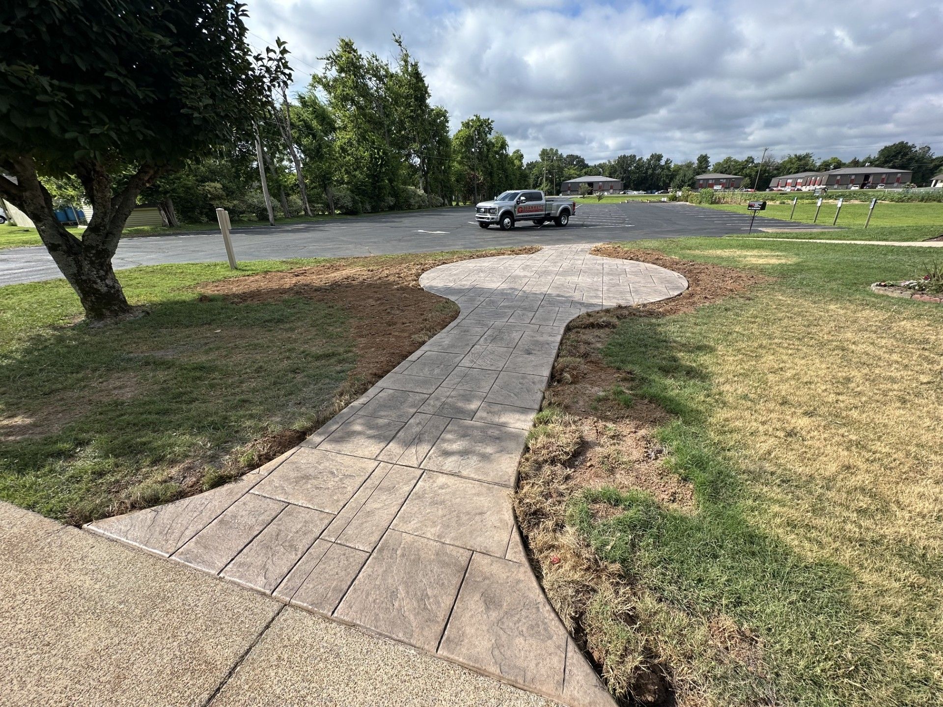 A concrete walkway leads to a parking lot with a truck parked.