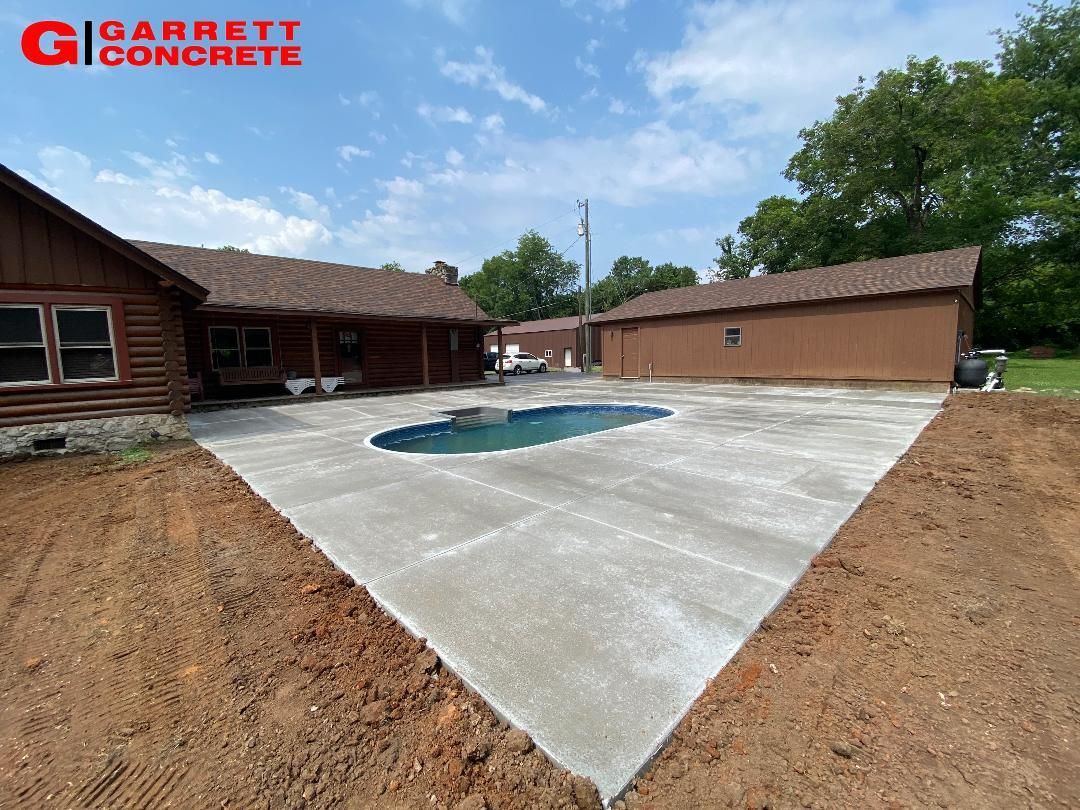 a concrete patio with a pool in the middle of it in front of a house