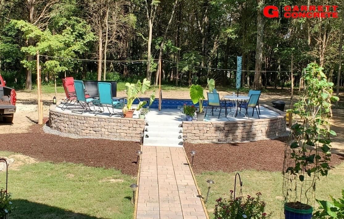 a patio area with a walkway leading to it and a swimming pool surrounded by trees