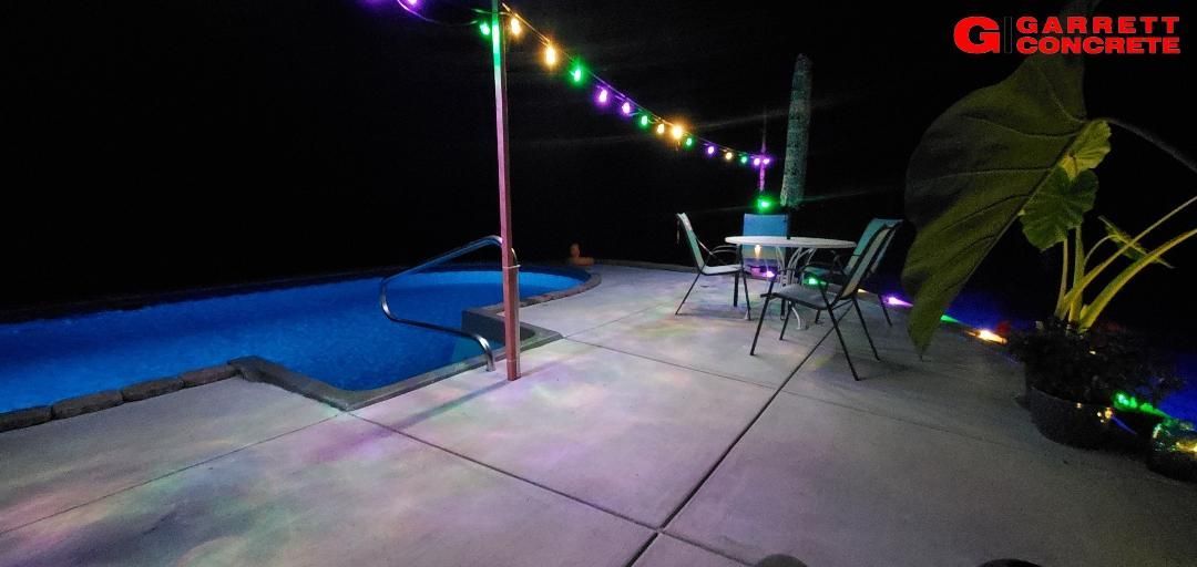 a patio with a table and chairs next to a pool at night