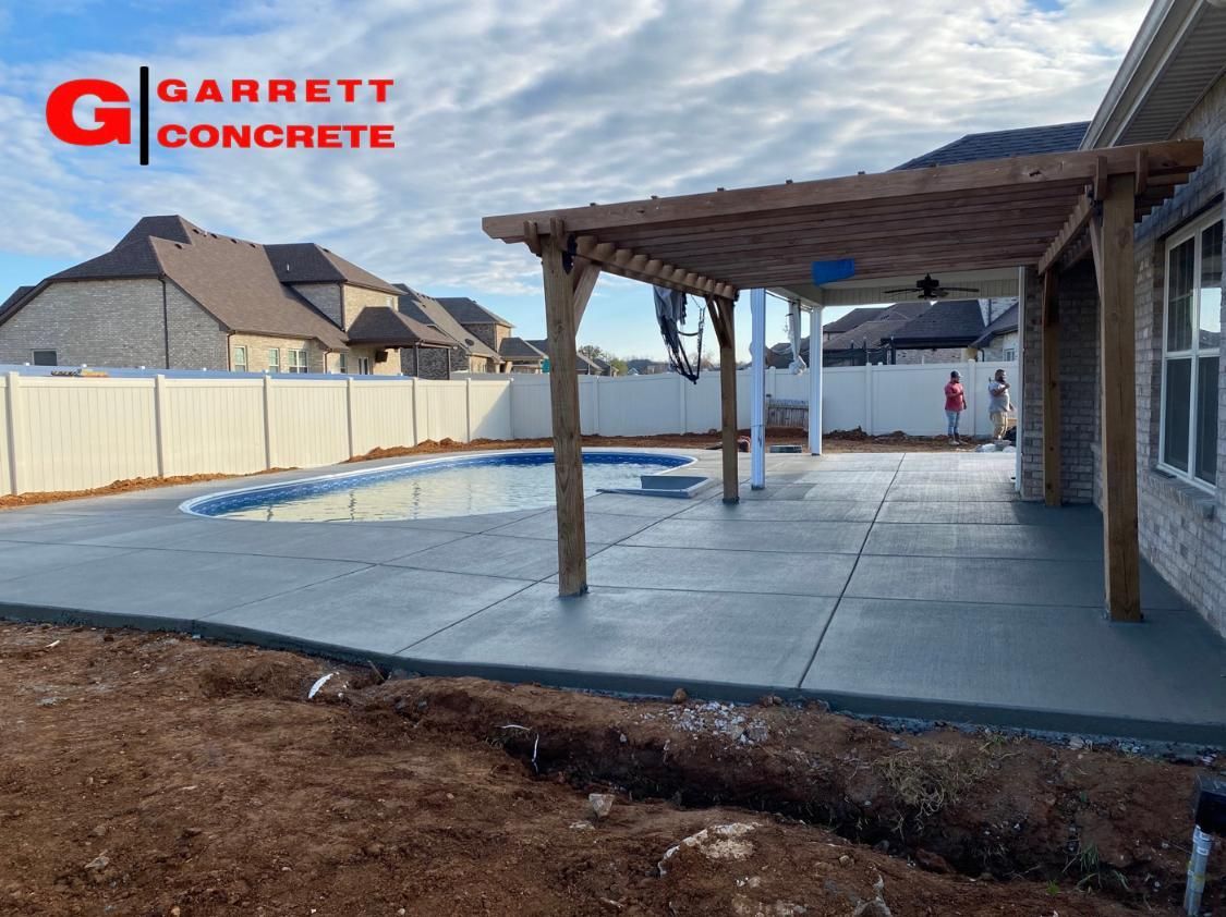 a patio with a pergola and a pool is being built by garrett concrete