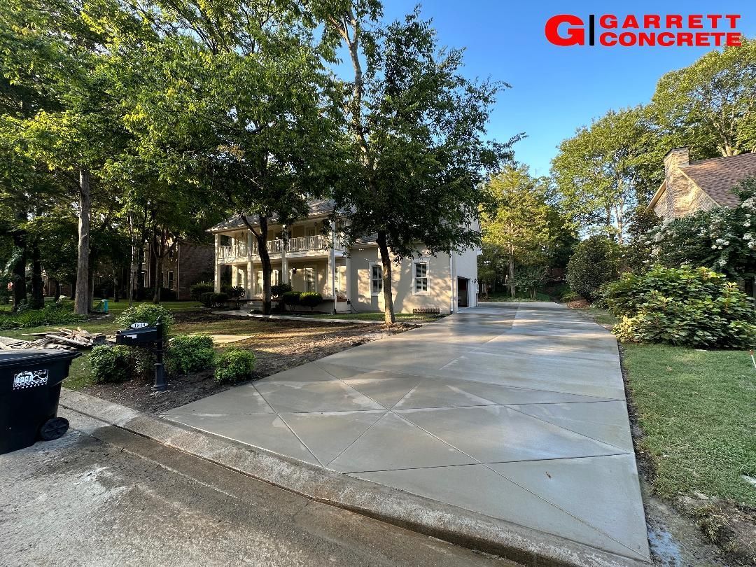 a concrete driveway leading to a house with trees in the background