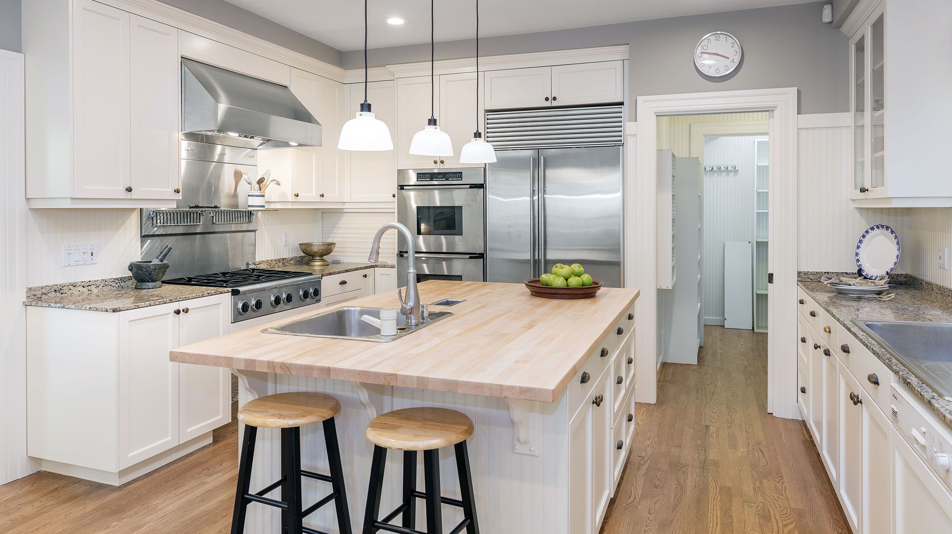 A kitchen with white cabinets , wooden counter tops , stainless steel appliances , and a large island.