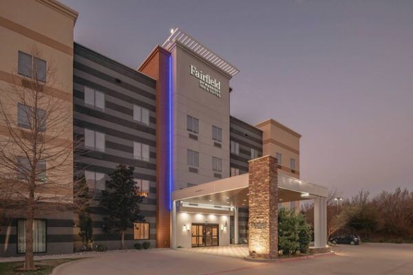 Fairfield Inn hotel exterior with lit entrance at dusk; grey, tan, and blue facade.
