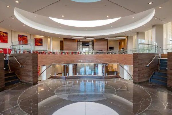 Grand, modern lobby with a curved ceiling, marble floors, and a balcony overlooking a seating area.
