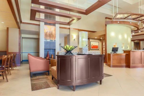 Hotel lobby with reception desk, seating area, and overhead lighting; neutral tones.