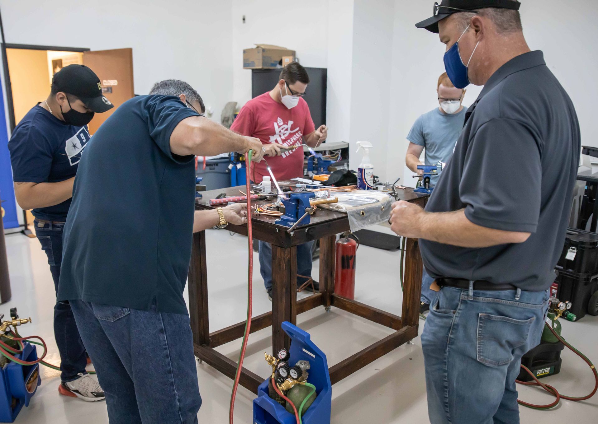 People working on equipment in a workshop. Men wearing masks work at a workbench with tools and gas tanks.