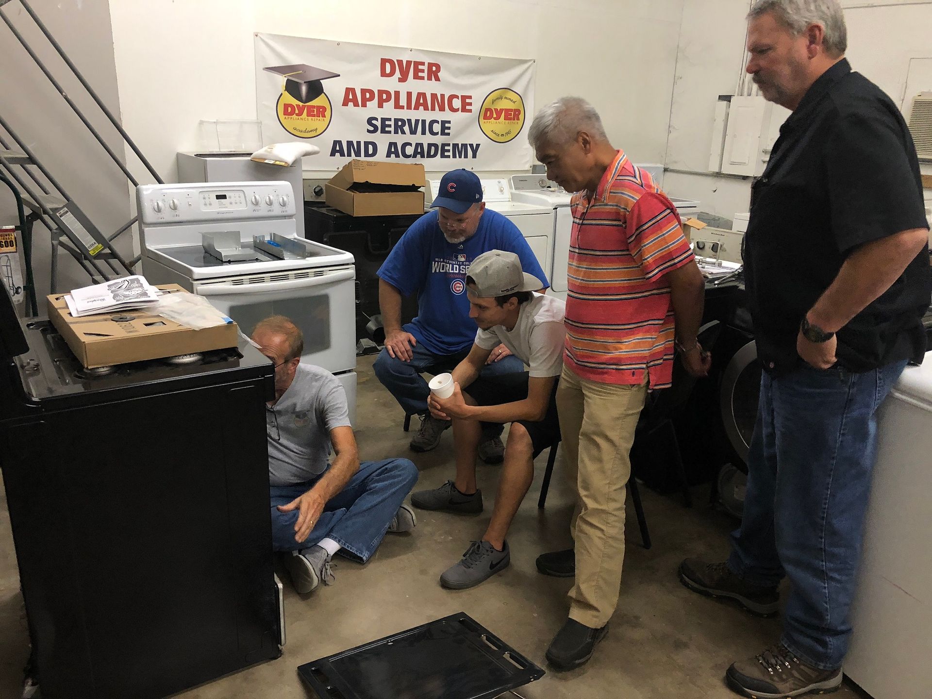 People gather around a black appliance. Workshop setting with appliances.