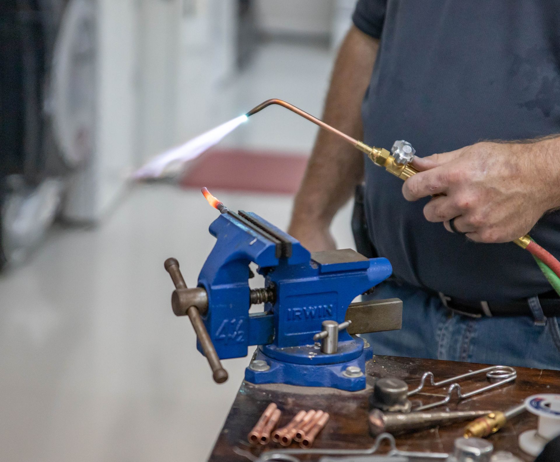 Person using a torch to solder copper pipe held in a blue vise on a wooden table.