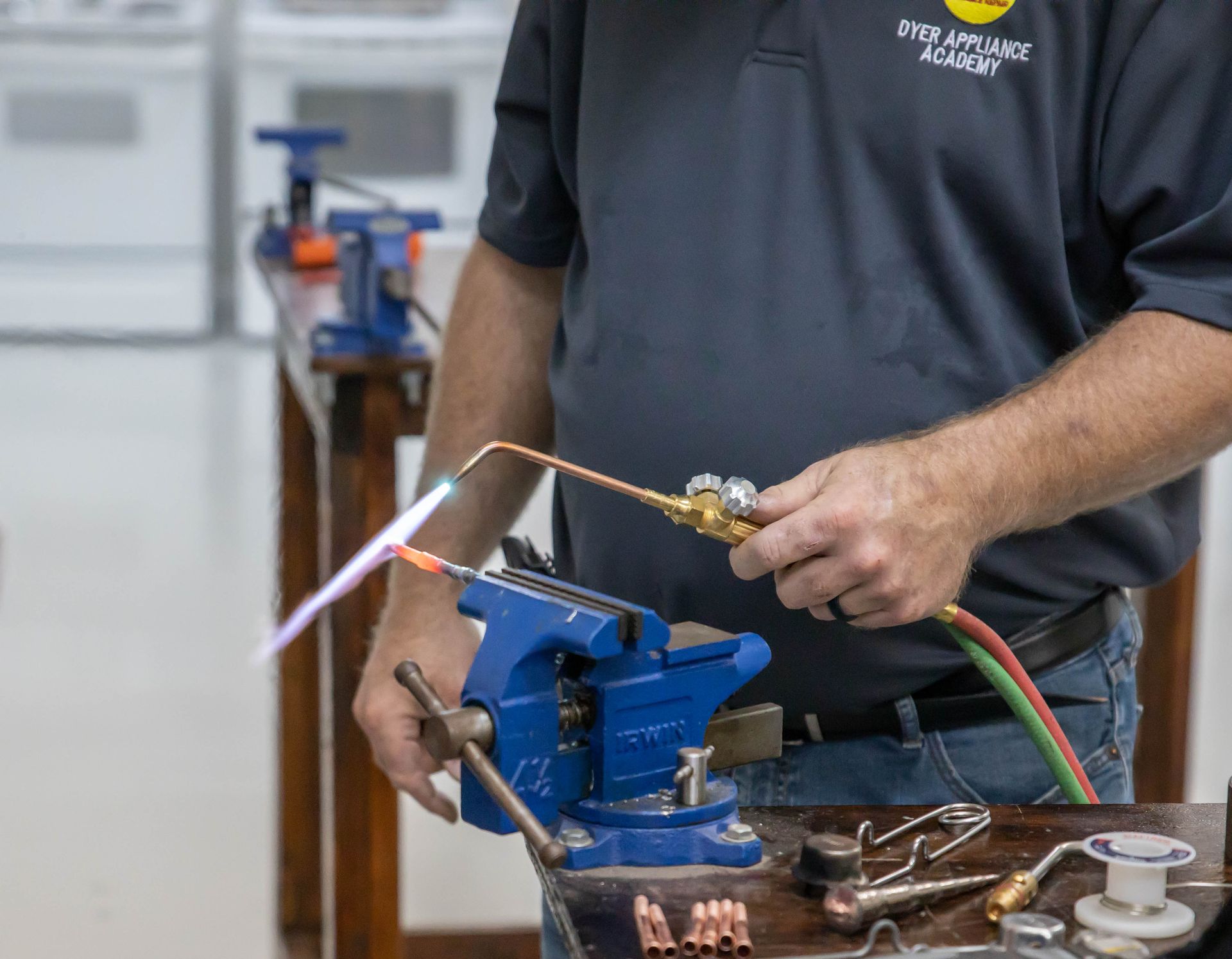 Person using a torch to solder copper pipes clamped in a vise.