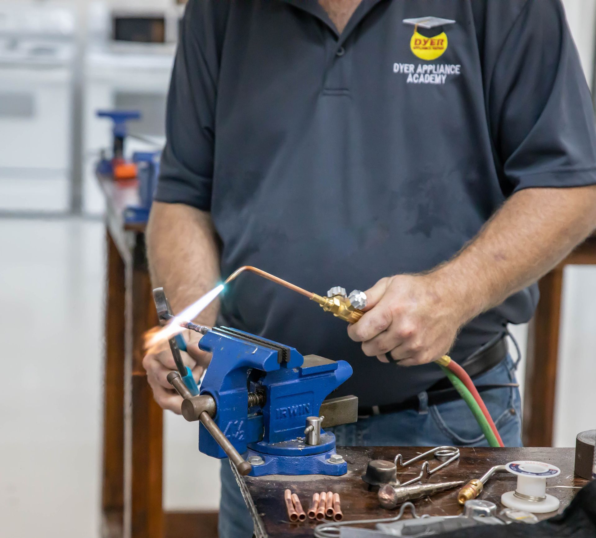 Person soldering copper pipes in a workshop, using a torch and vise.