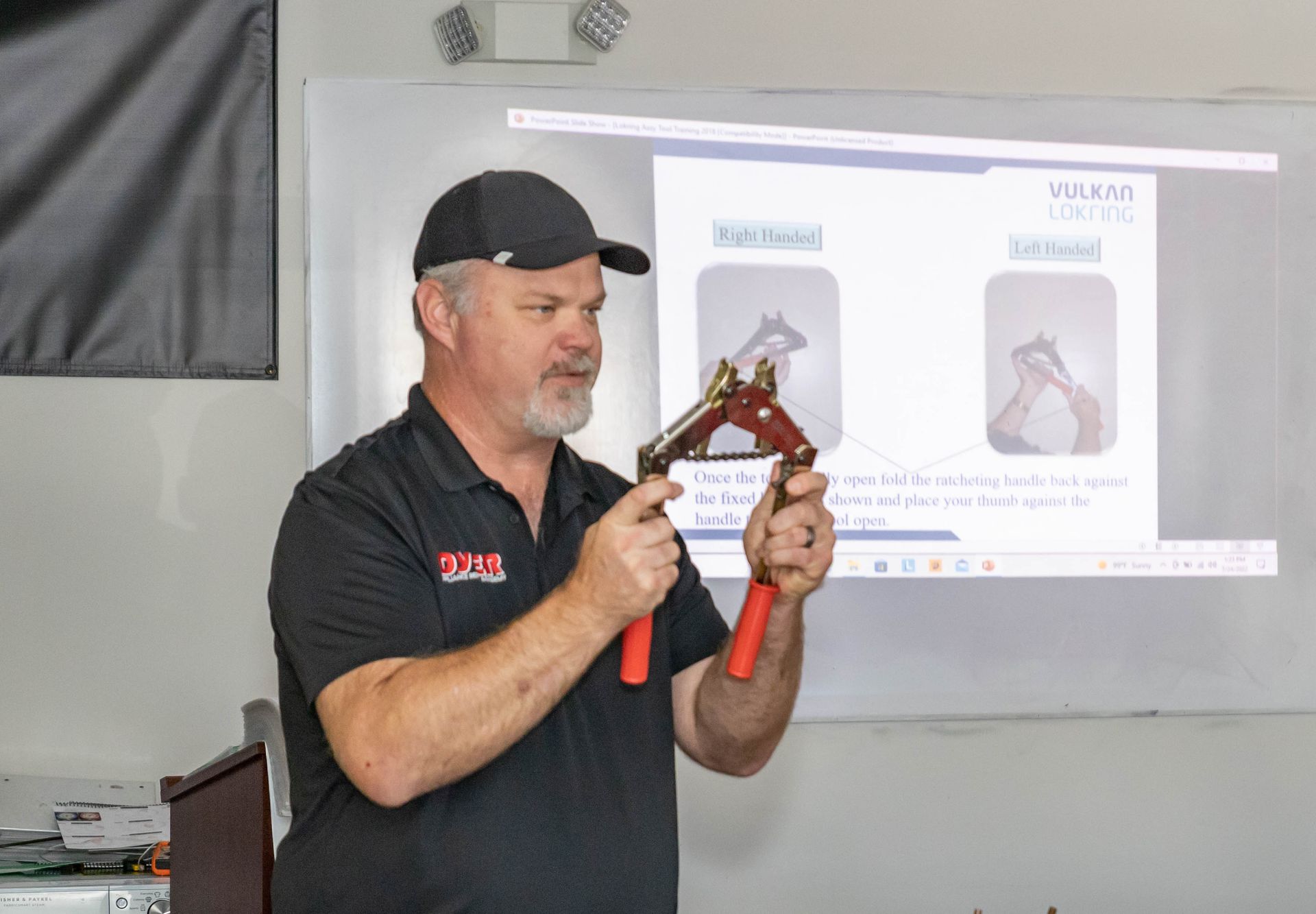 Man holding tool, presenting in a classroom. PowerPoint shows equine feet.