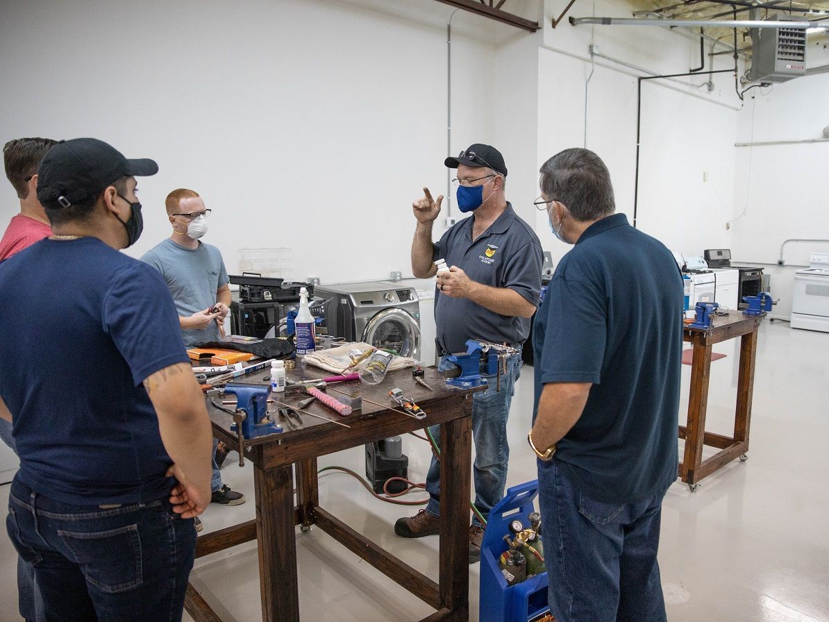 Group of people in a workshop, instructor gesturing, tools on tables.
