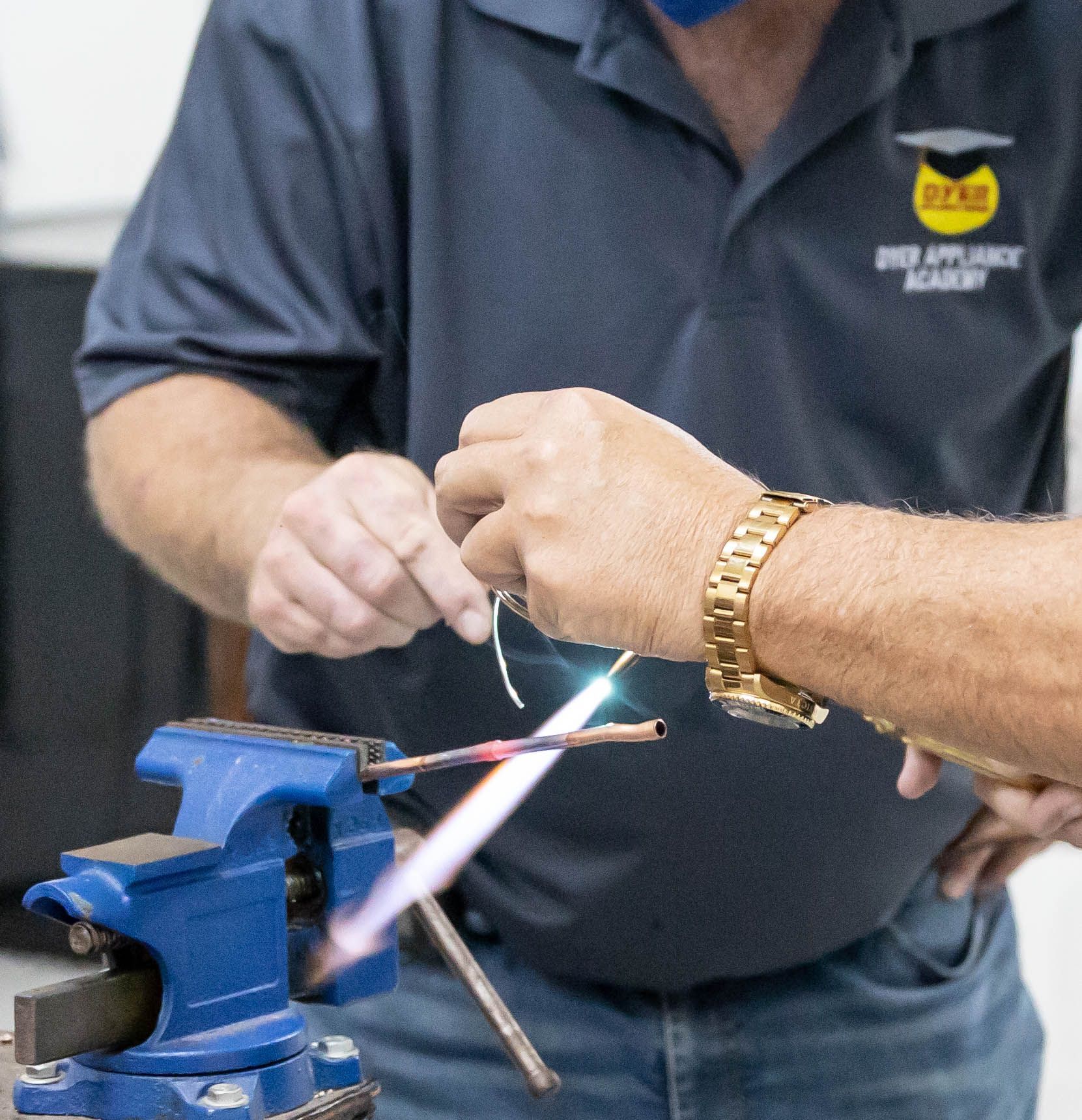 Person soldering copper pipes with a torch. Blue vice grips hold the pipes.