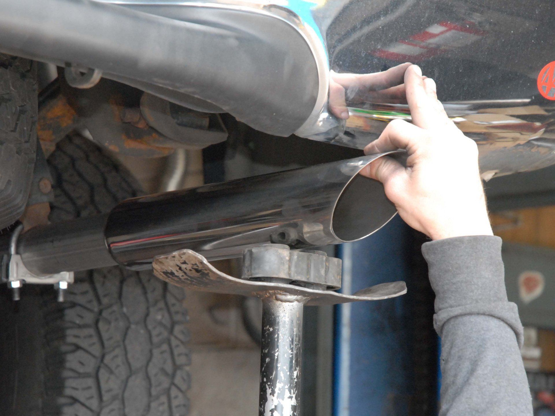 Person installing a black exhaust pipe on a car, reaching with hand.