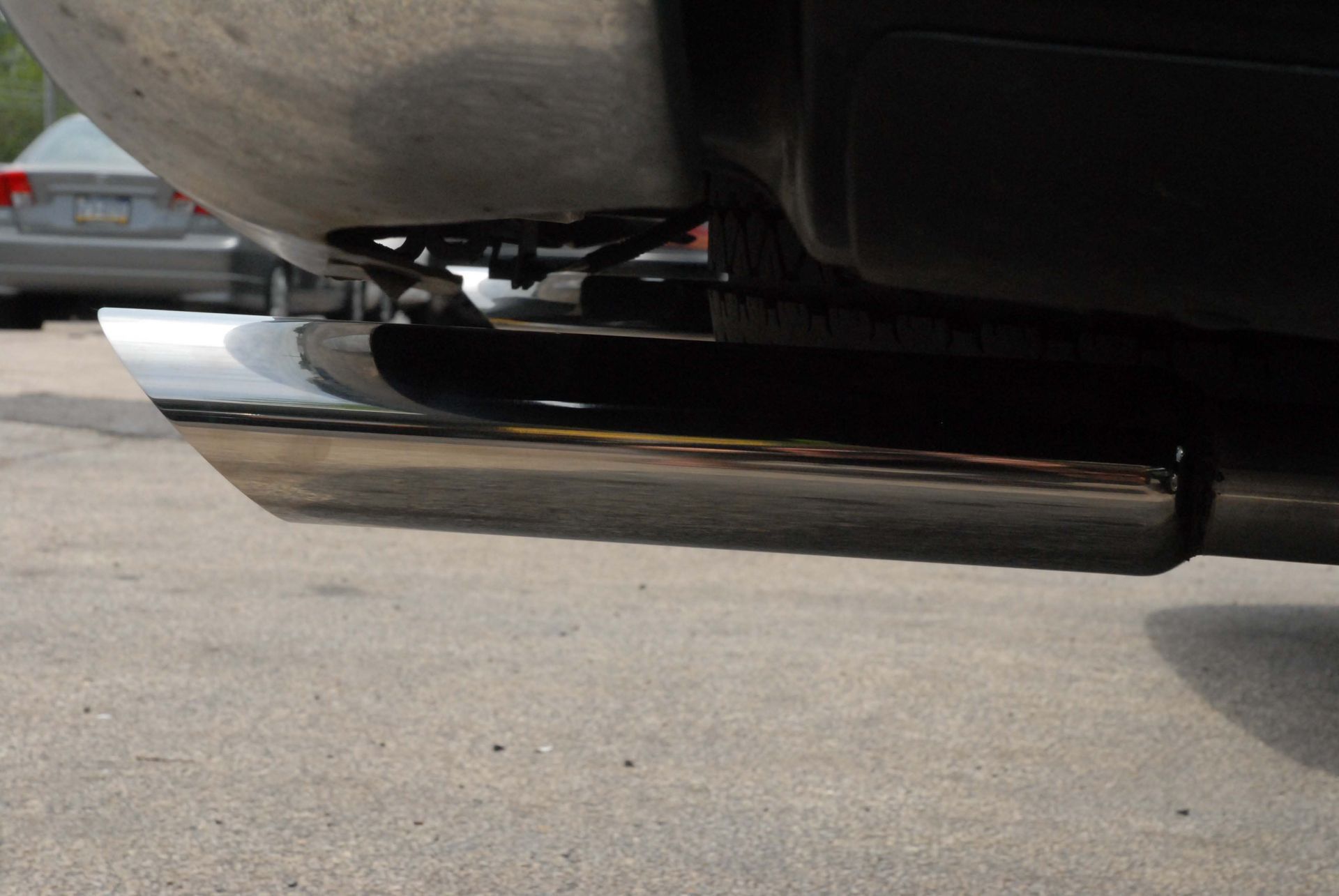 Chrome exhaust pipe extending from a vehicle's rear, reflecting the environment.