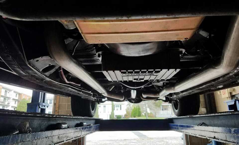 Underside of a vehicle on a lift, showing chassis, exhaust, and protective plates.