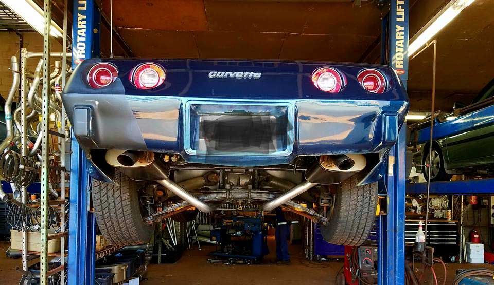 Underside of a red car showing exhaust pipes, muffler, and suspension components.
