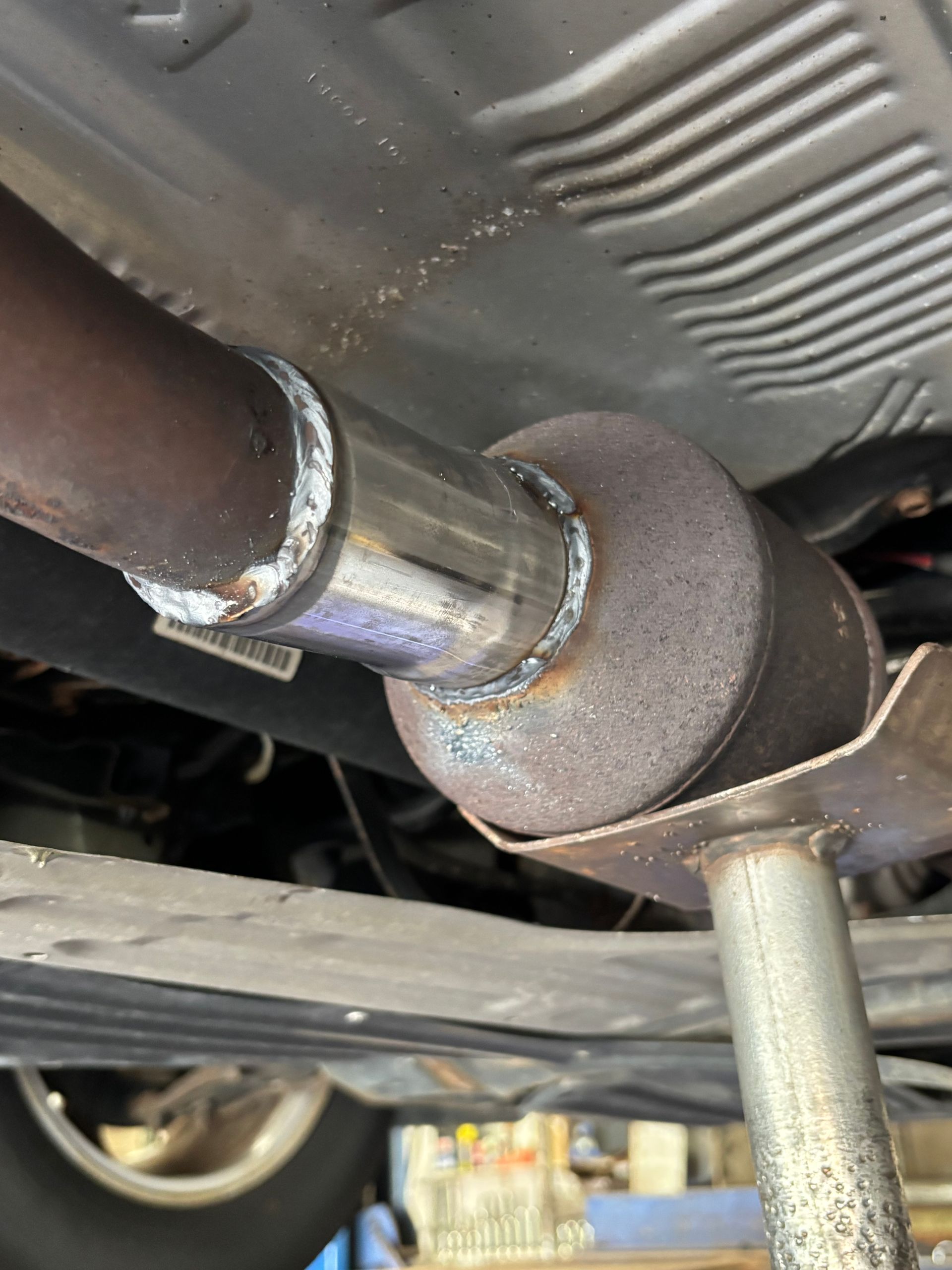 Exhaust pipe welded to a catalytic converter, viewed from underneath a vehicle.