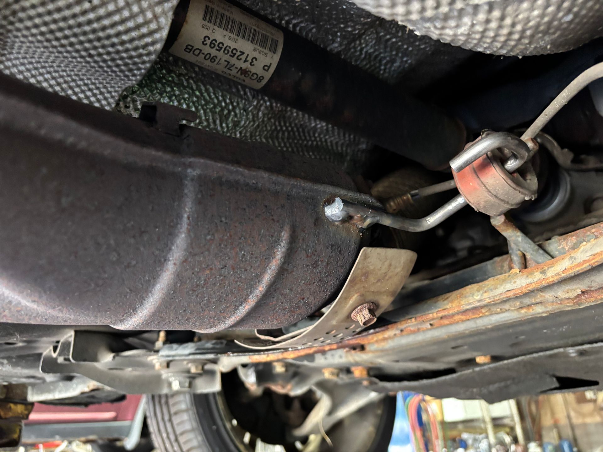 Undercarriage of a vehicle. Exhaust pipe, heat shield, and suspension components visible.
