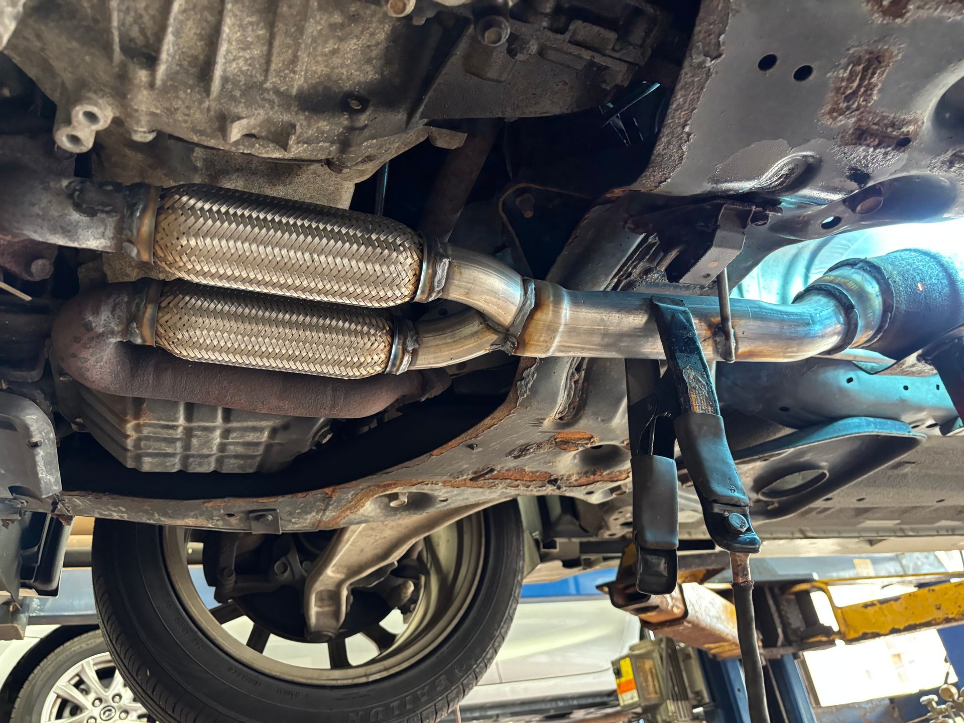 Undercarriage of a vehicle; exhaust system repair. Metal exhaust pipes, flexible joints, undercarriage rust, and car jack.