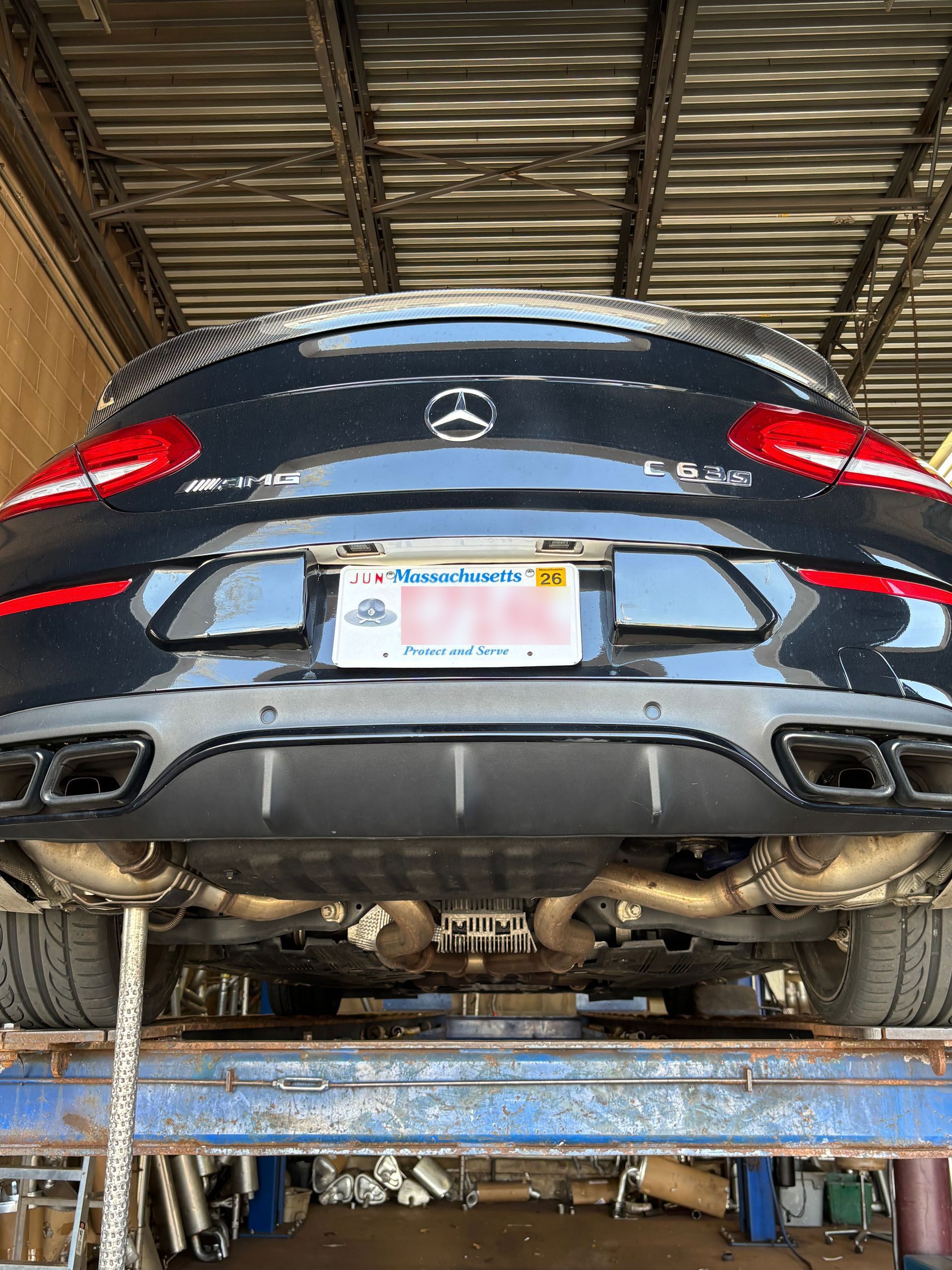 Black Mercedes-AMG C 63 S sedan on a lift, showing the exhaust system and Massachusetts license plate.