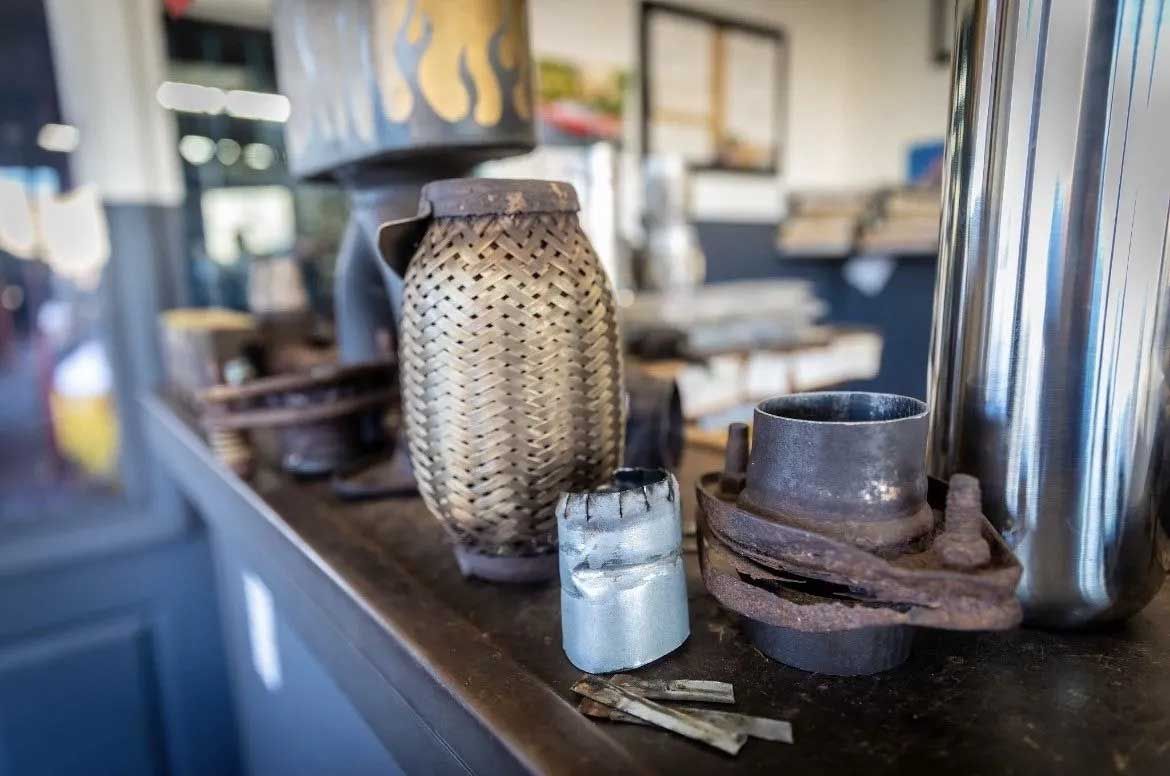 Rusty car exhaust parts on a shelf; a mesh pipe, flanges, and other components are visible indoors.