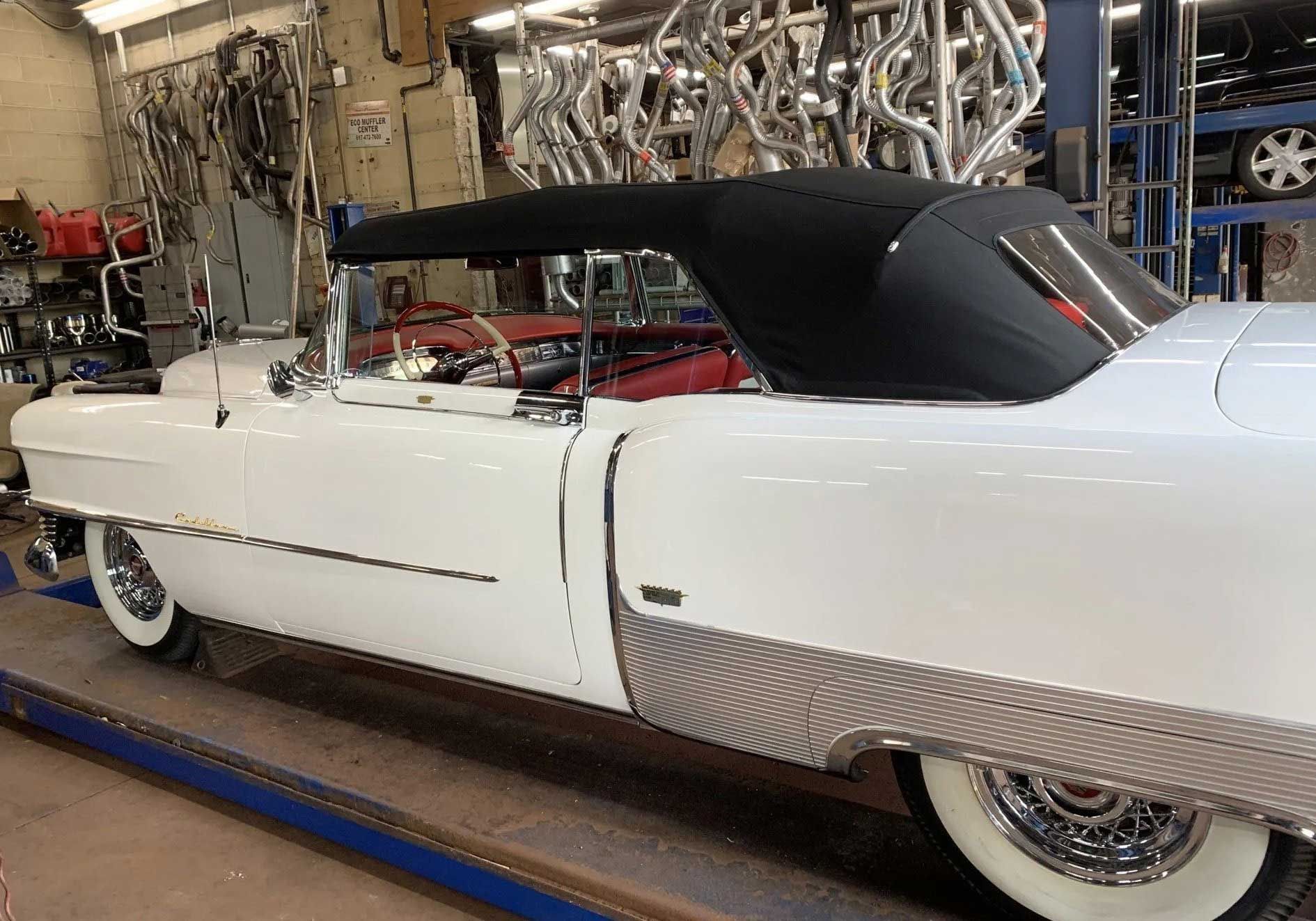 White classic convertible car with a black top in a garage setting.