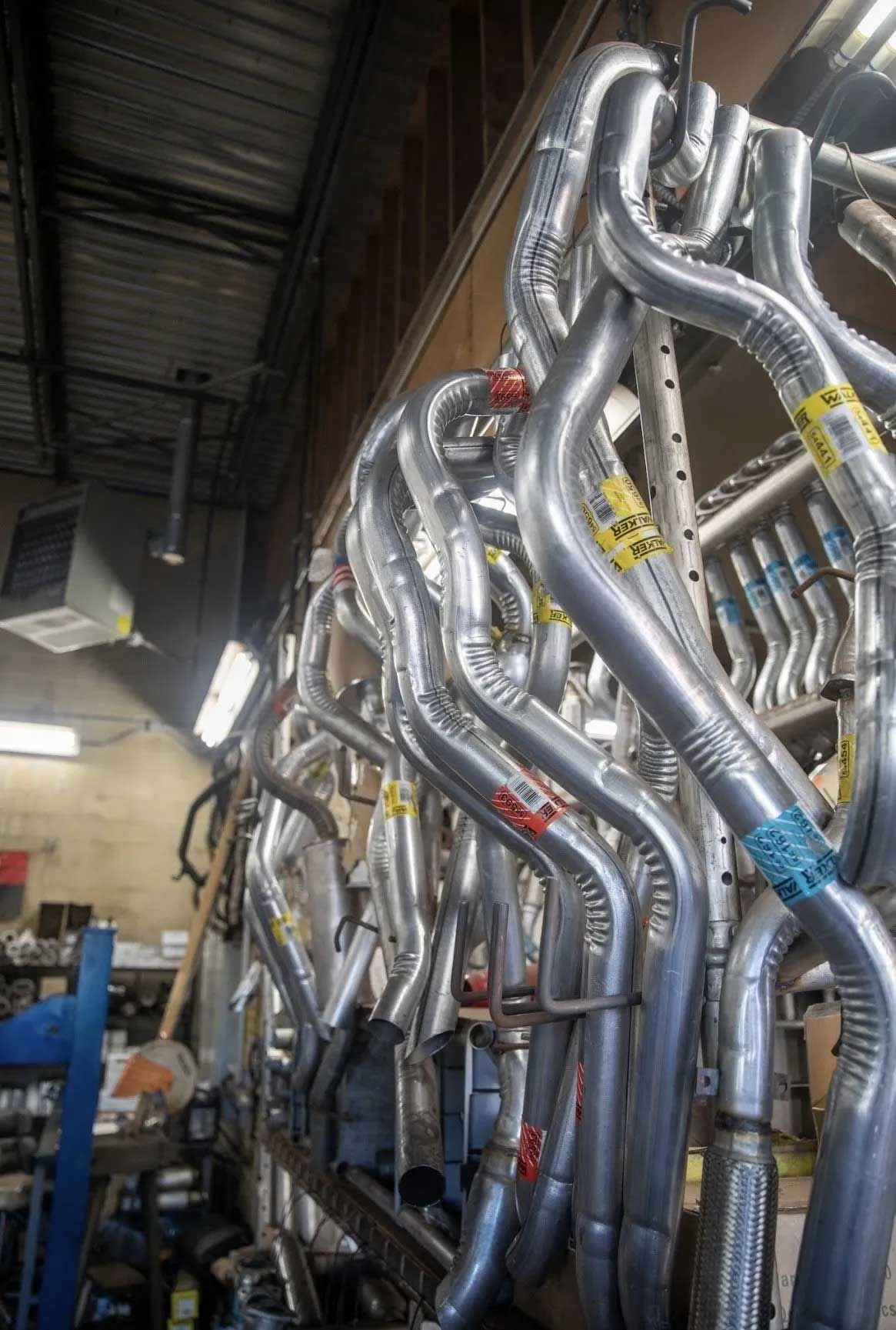 Metal exhaust headers hanging in a workshop. Silver pipes with colored labels.
