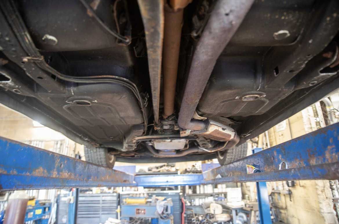 Underside of a car on a lift in a garage, showing exhaust system, driveshaft, and undercarriage.