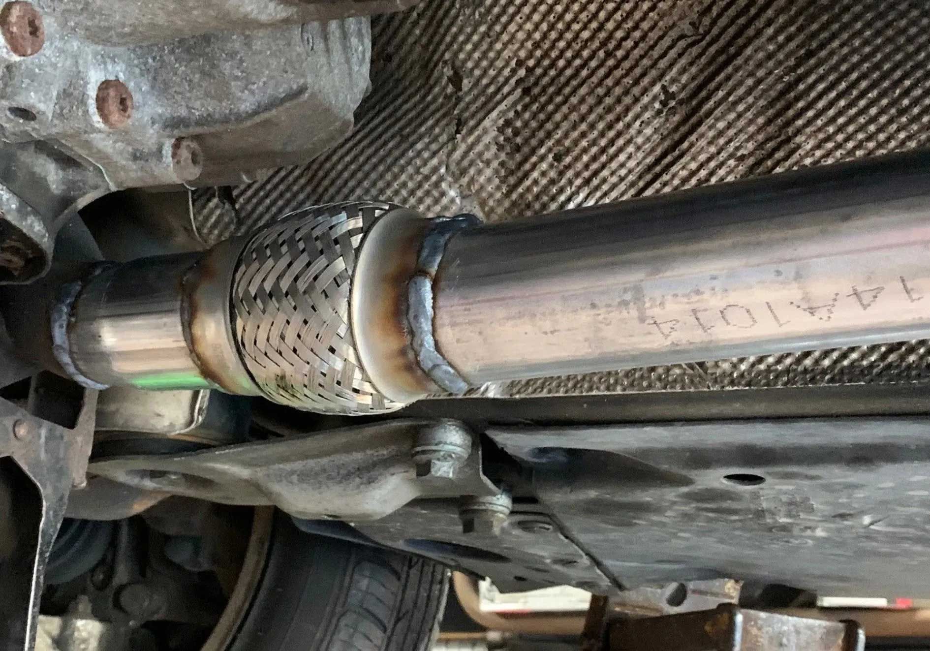 Undercarriage of a car showing a welded exhaust pipe with a flexible section.