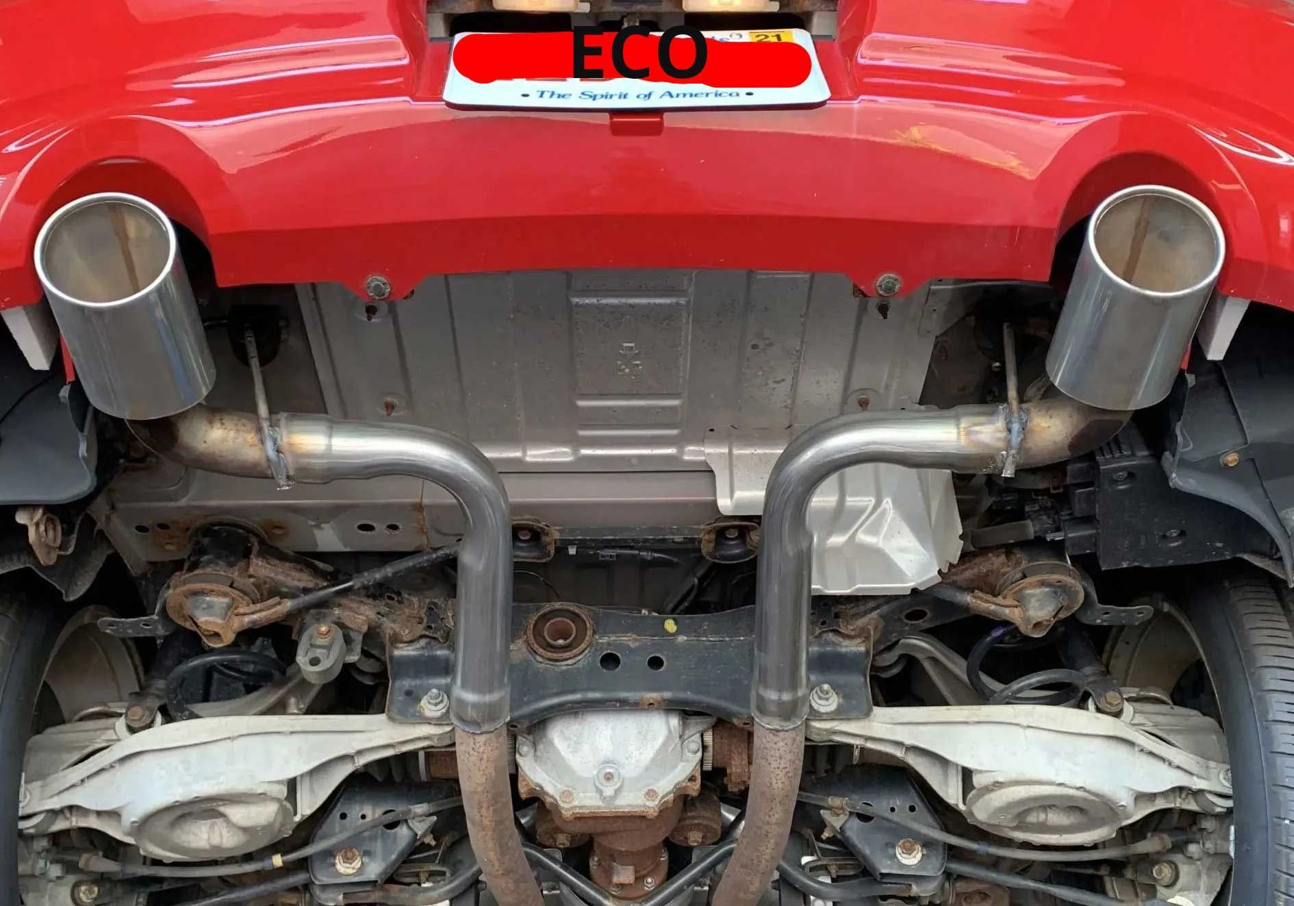 Underside of a red car showing exhaust pipes, muffler, and suspension components. The car is parked, viewed from below.
