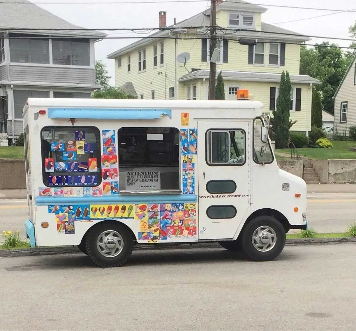 Ice cream truck parked on a street. White vehicle with colorful ice cream graphics and a serving window.
