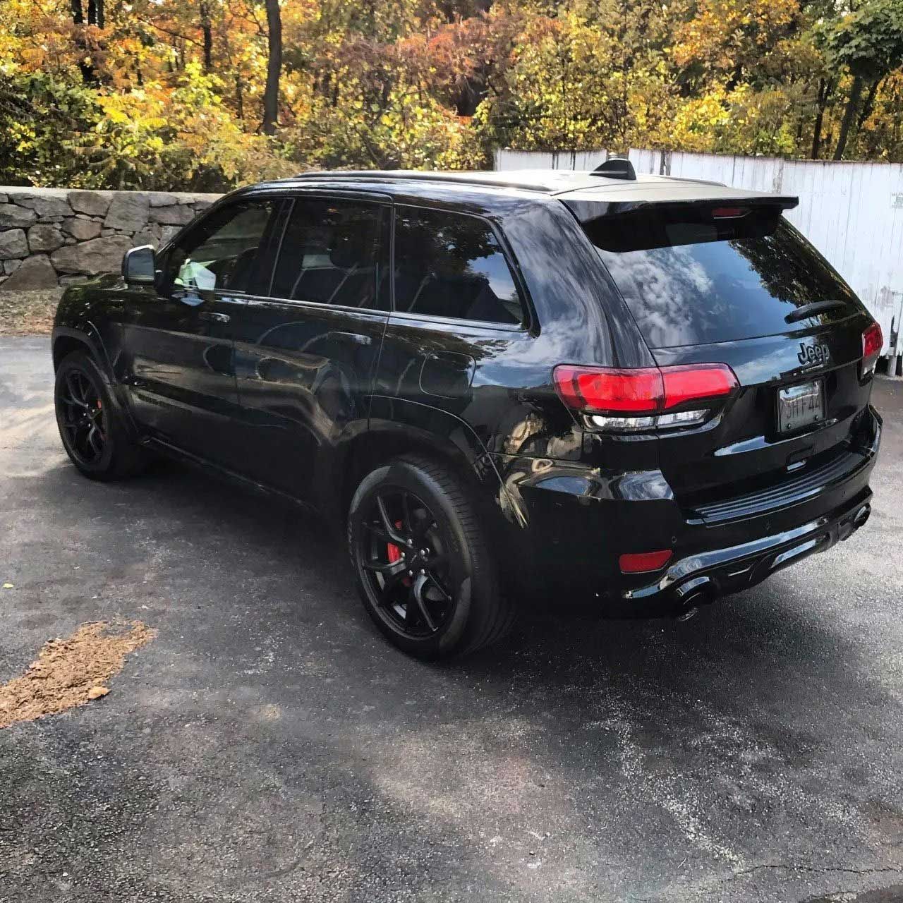 Black Jeep SUV parked on a paved surface with black rims, red brake calipers, and fall foliage in background.