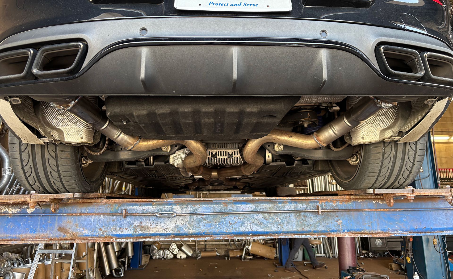 Undercarriage of a black car on a lift. Exhaust system visible; brown pipes, black mufflers.