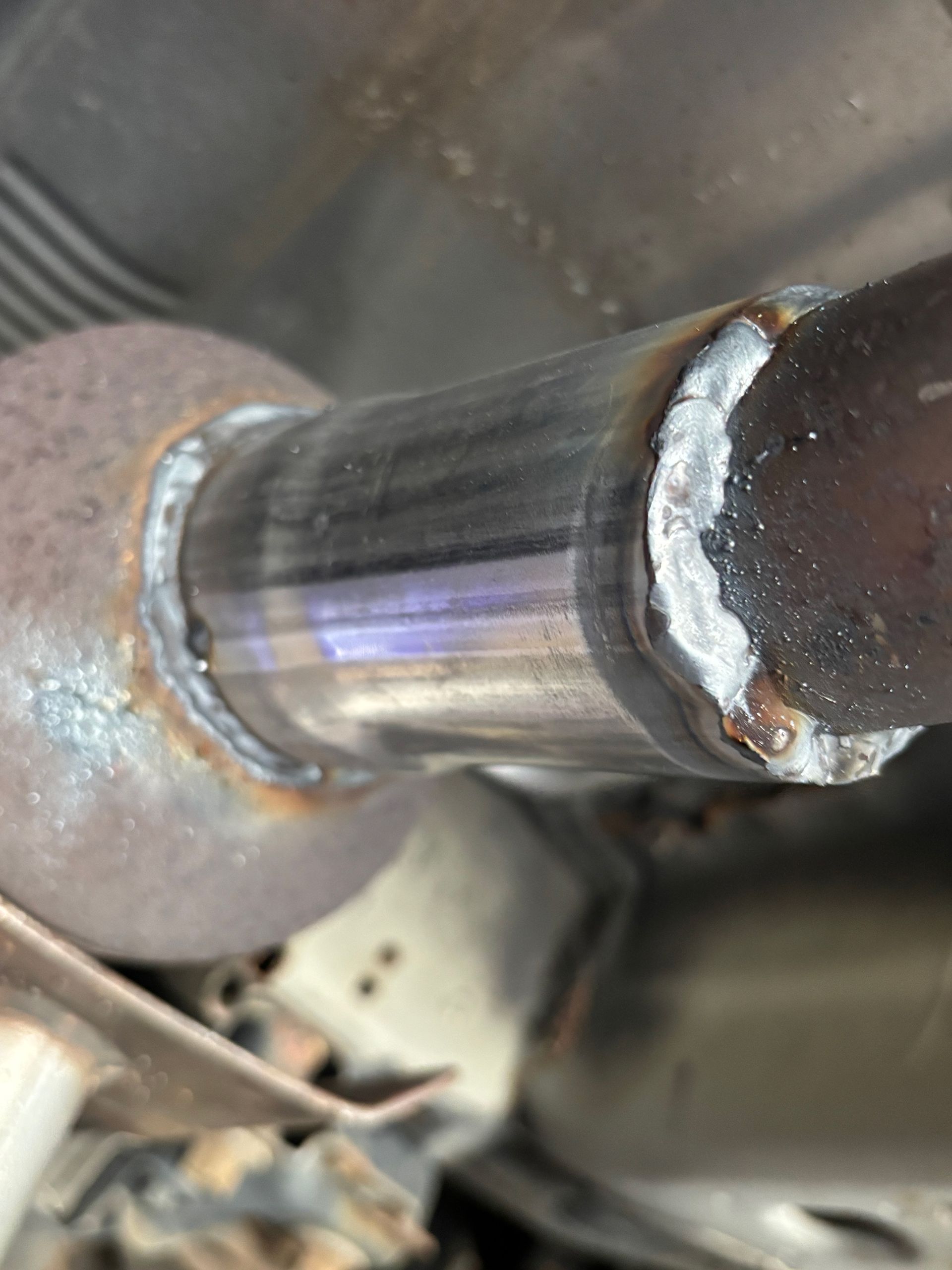 Close-up of a car exhaust pipe weld, showing two pieces of metal joined by a gray weld with visible seams.