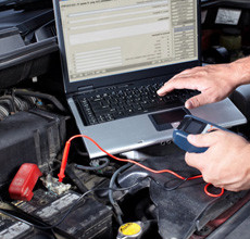 A person is working on a laptop computer under the hood of a car.