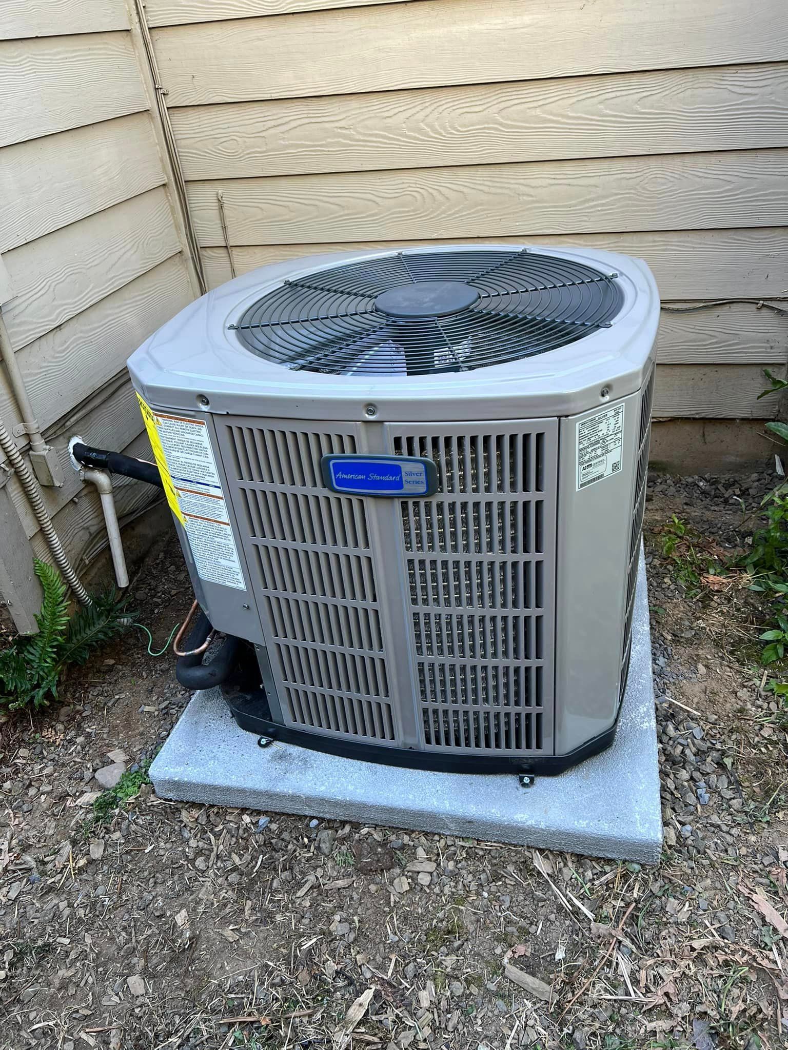 A large air conditioner is sitting on top of a gravel covered ground in front of a house.