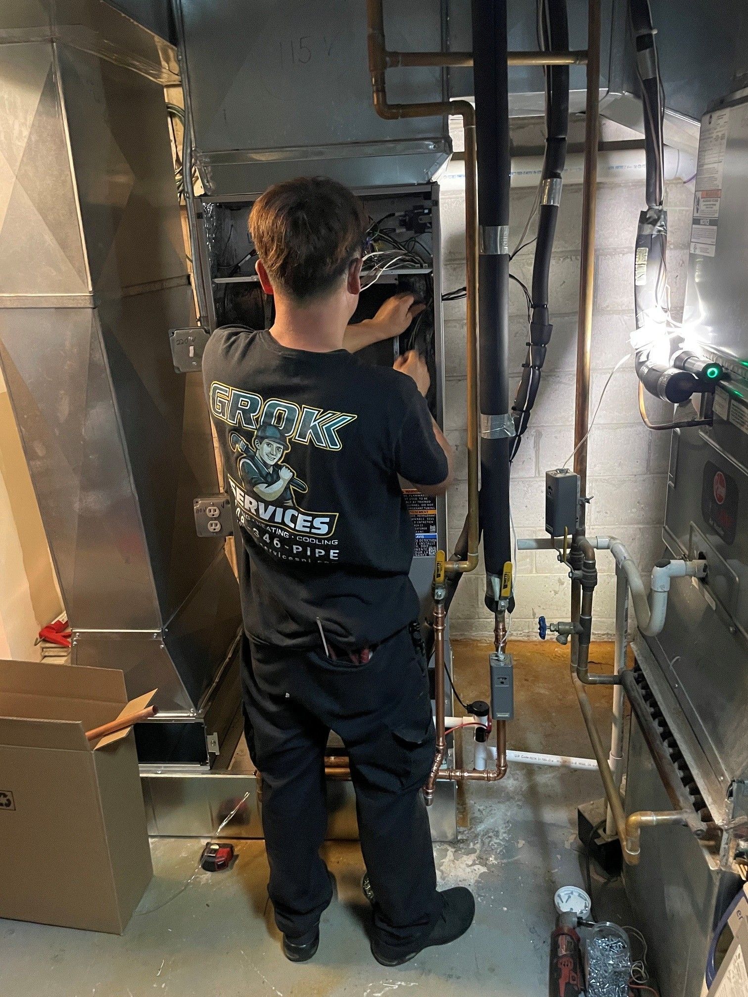 Worker standing in a narrow industrial duct area, inspecting equipment in a metal utility space.
