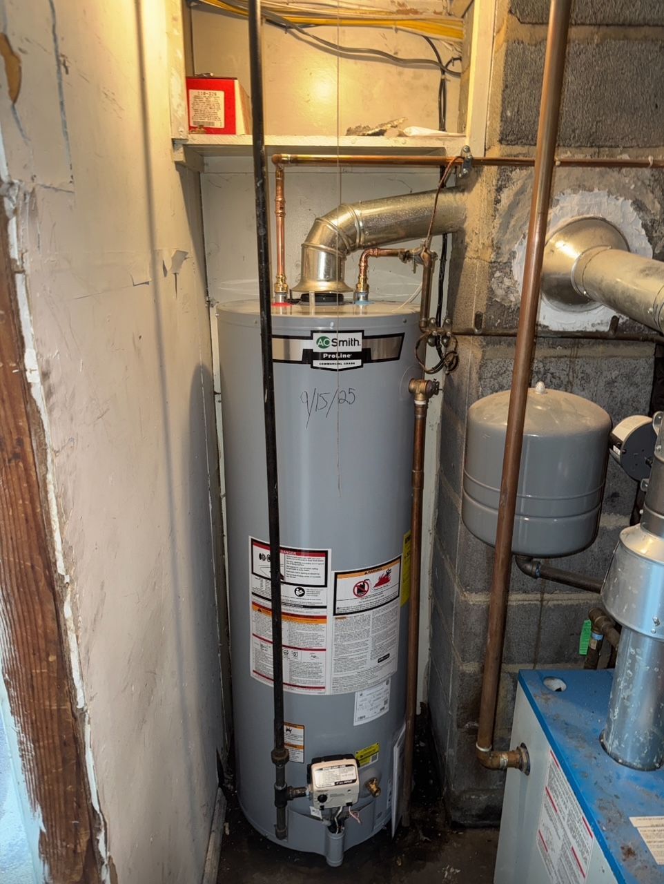 a vertical water heater in a small, enclosed space with copper pipes and a vent