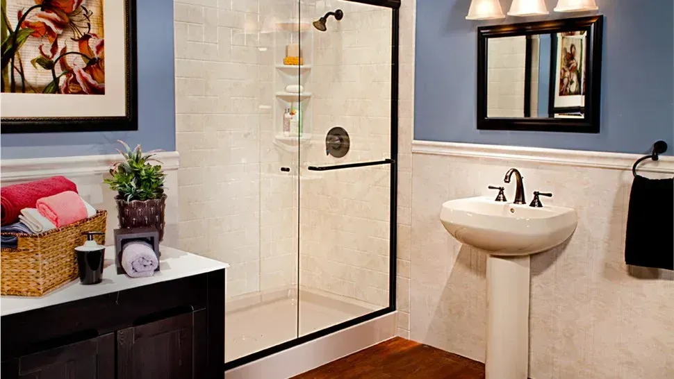 Modern bathroom with glass shower, white pedestal sink, black vanity, and blue walls