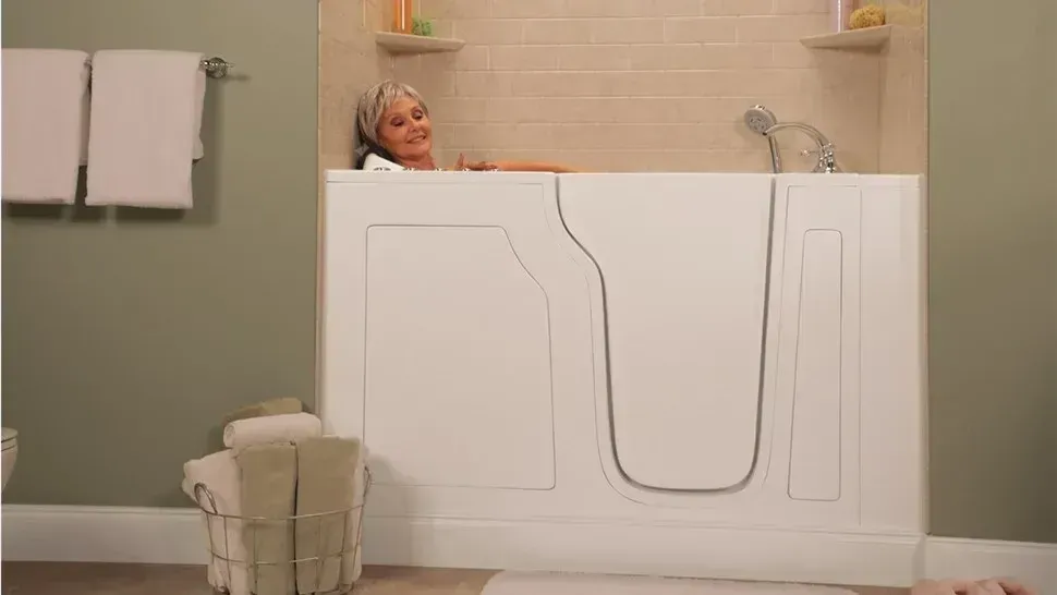 Person relaxing in a bathtub behind a white bath panel in a beige bathroom.