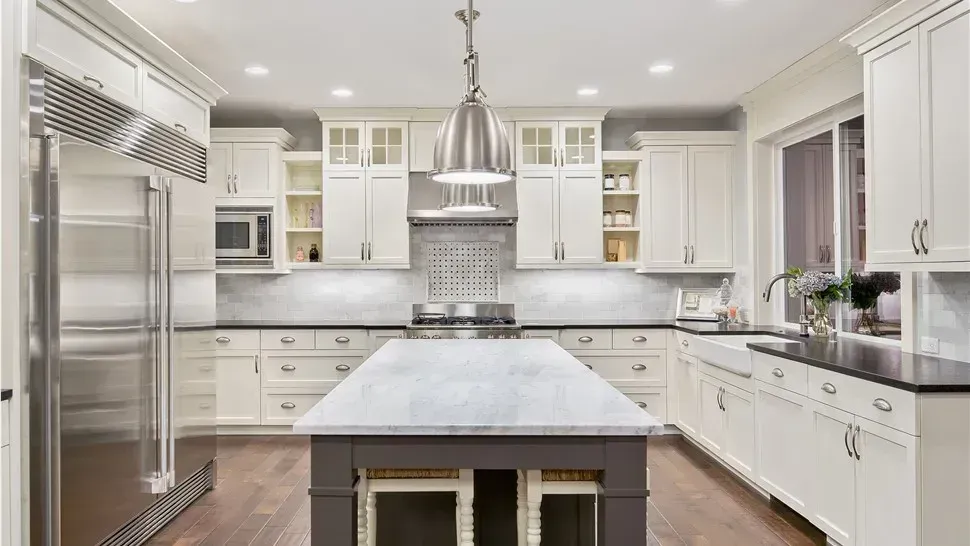 Bright white gourmet kitchen with marble island, stainless steel appliances, and dark wood floors