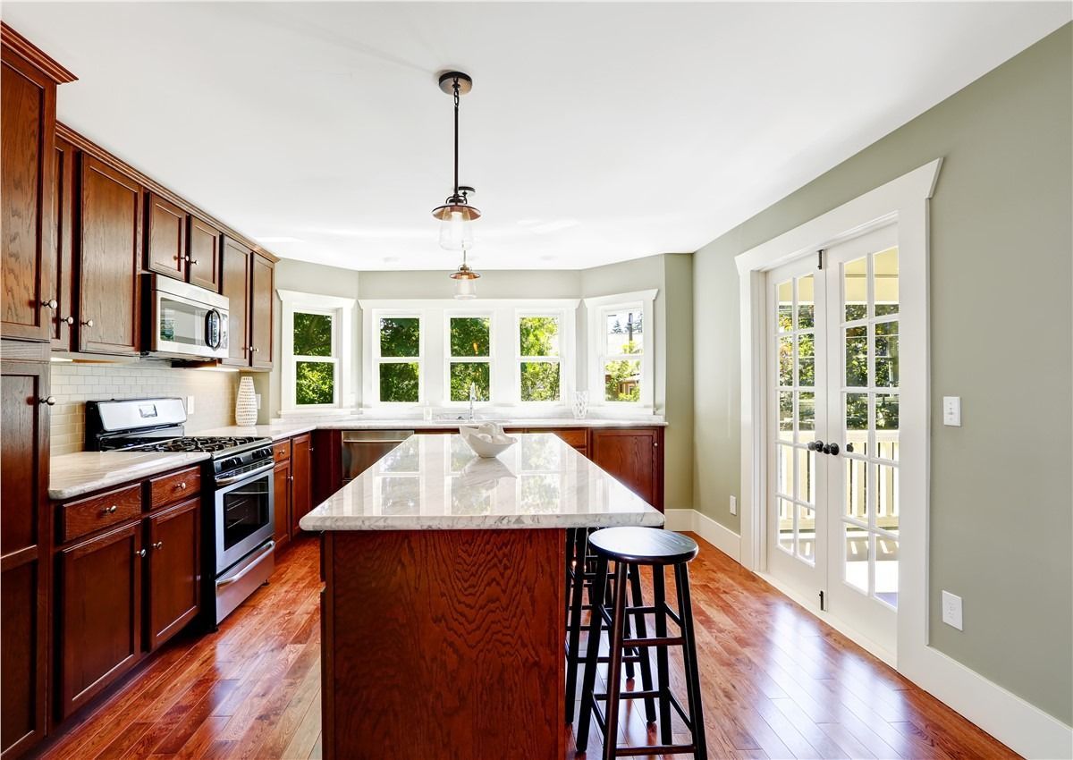 Bright kitchen with dark wood cabinets, granite island, hardwood floors, and French doors to the right