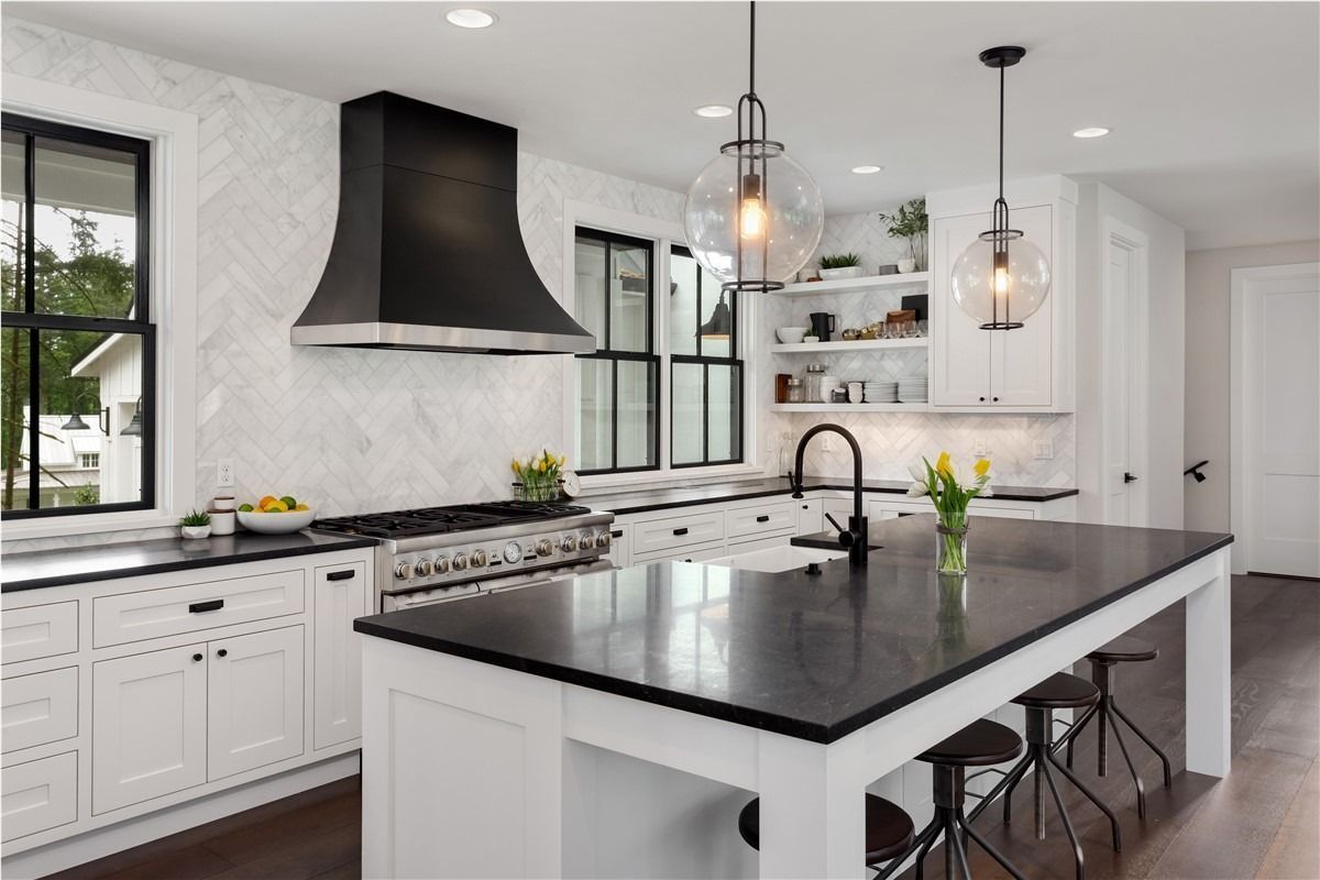 Modern white kitchen with black island countertop, pendant lights, and stainless range hood