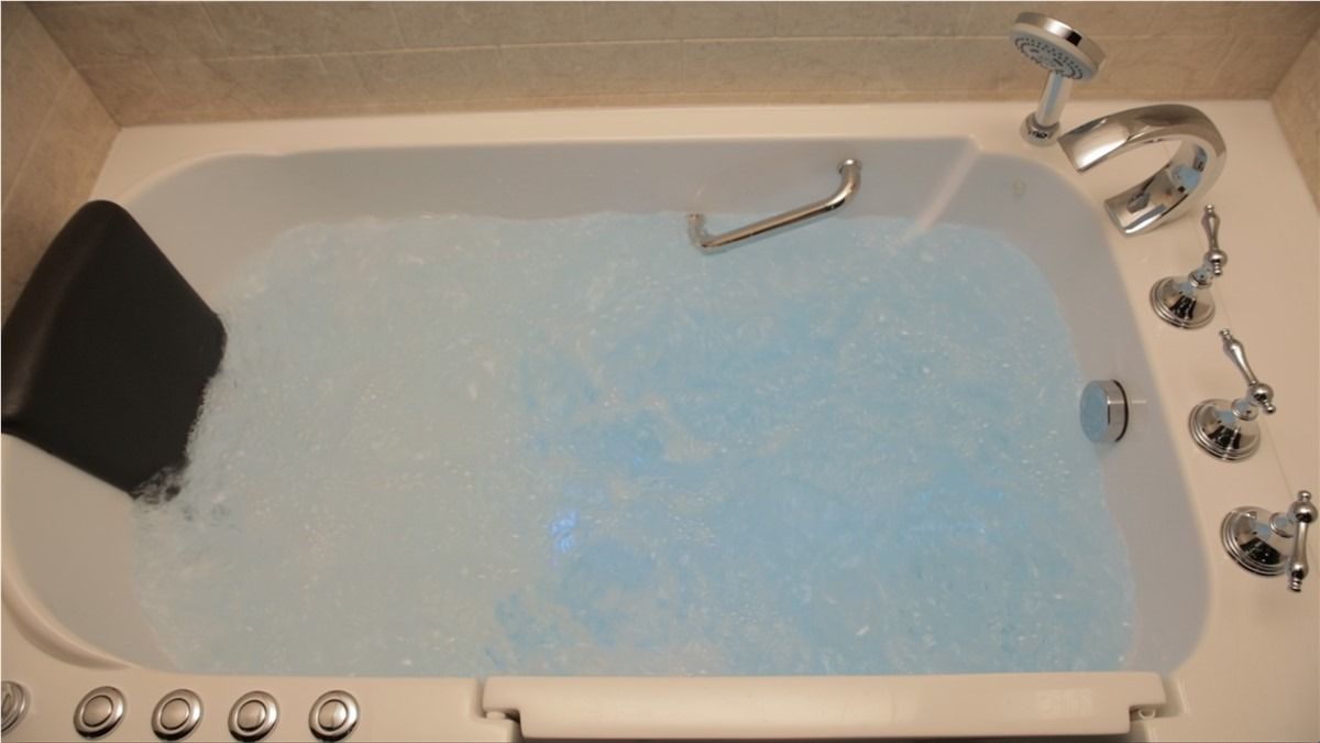 Bathtub filled with pale blue water, with faucet and shower controls visible.