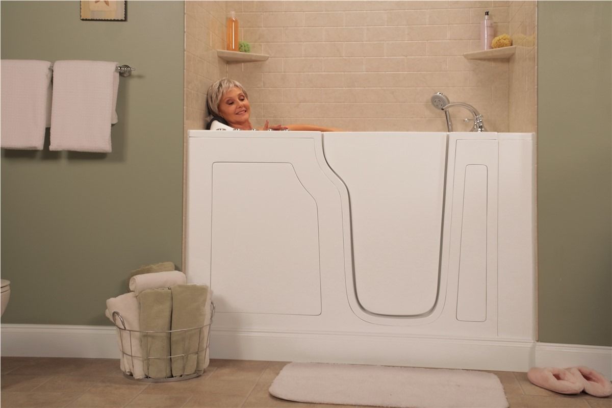 Person relaxing in a white freestanding tub in a beige bathroom with towels and candles